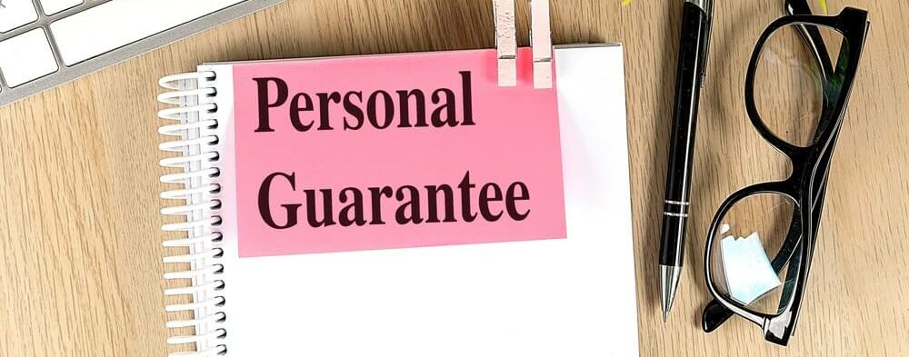 PERSONAL GUARANTEE text pink sticky on a notebook with keyboard, pen and glasses .